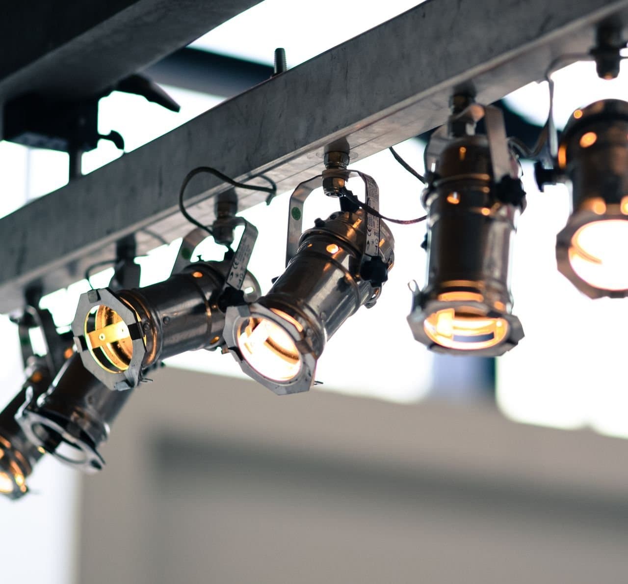 Row of black directional spotlights mounted on an industrial track, glowing warm against a dark ceiling
