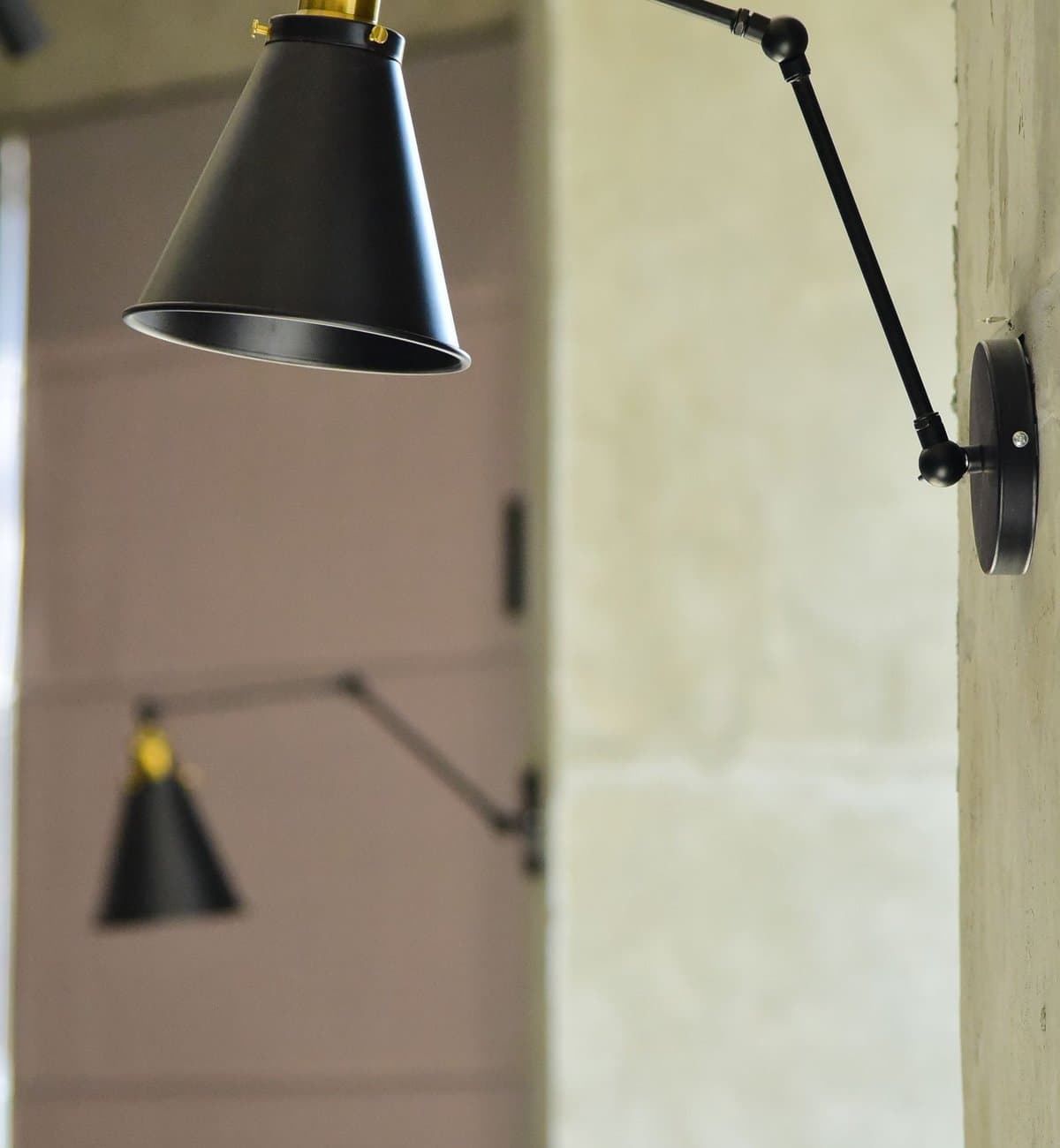 Black adjustable swing-arm wall lamps with conical shades on a stone wall